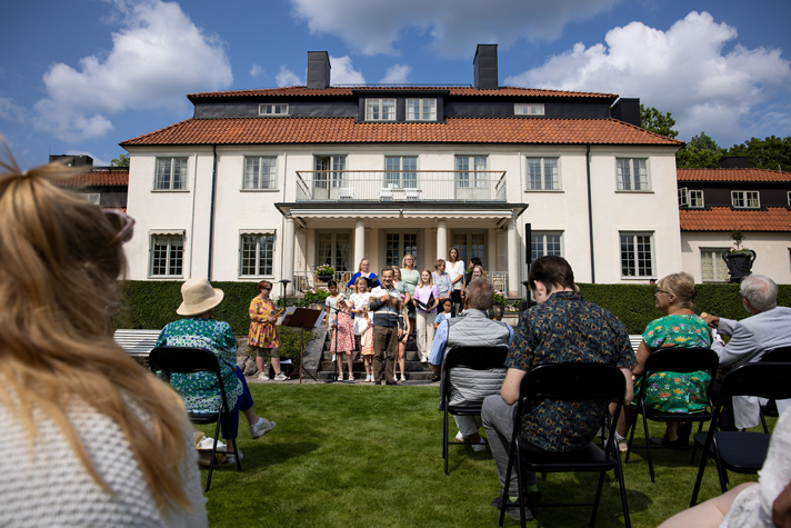 Ståtlig vit byggnad, rader med publik, barn som sjunger. 