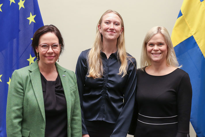 Maria Malmer Stenergard, Clara Werner och Paulina Brandberg står framför en EU-flagga och en svenska flagga.