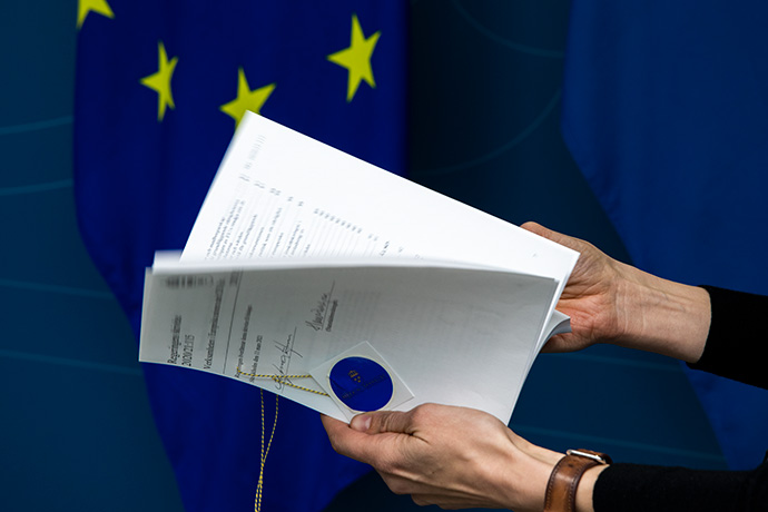 En hand bläddrar i Årsboken om EU, i bakgrunden syns EU:s flagga En hand bläddrar i Årsboken om EU, i bakgrunden syns EU:s flagga