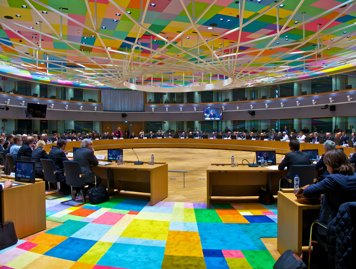 Rådets möteslokal i Bryssel med en matta i många färger och många personer i rummet.