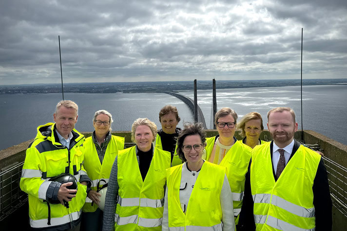 Nordiska ministrar står med samlade uppe på Öresundsbron. I bakgrunden syns bron och vattnet i resund.De har reflexvästar på sig