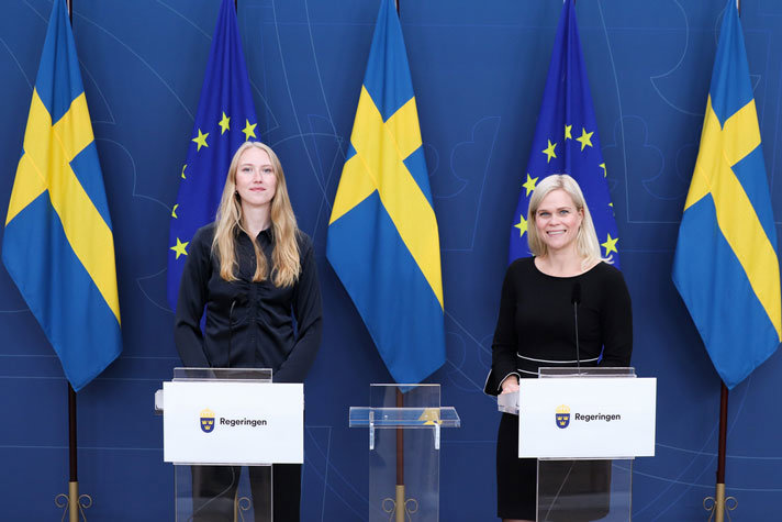 Clara Werner och Paulina Brandberg står i pressrummet på Rosenbad bakom varsitt ståbord. I bakgrunden syns svenska flaggor.