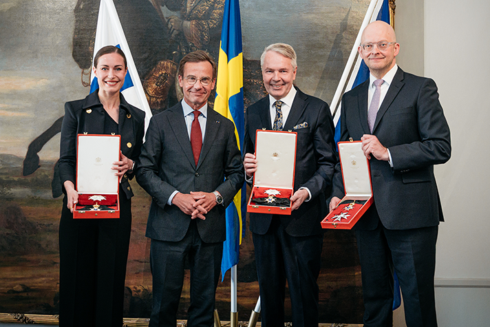 Sanna Marin, Ulf Kristersson, Pekka Haavisto och Petri Hakkarainen står bredvid varandra inomhus. Marin, Haavisto och Hakkarainen håller upp varsitt medaljetui. I bakgrunden syns finska flaggan, svenska flaggan och EU-flaggan.