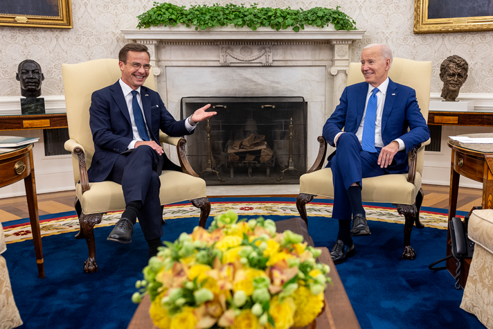 Statsminister Ulf Kristersson och president Joe Biden sitter vid en öppen spis i ett stort rum i vita huset. 