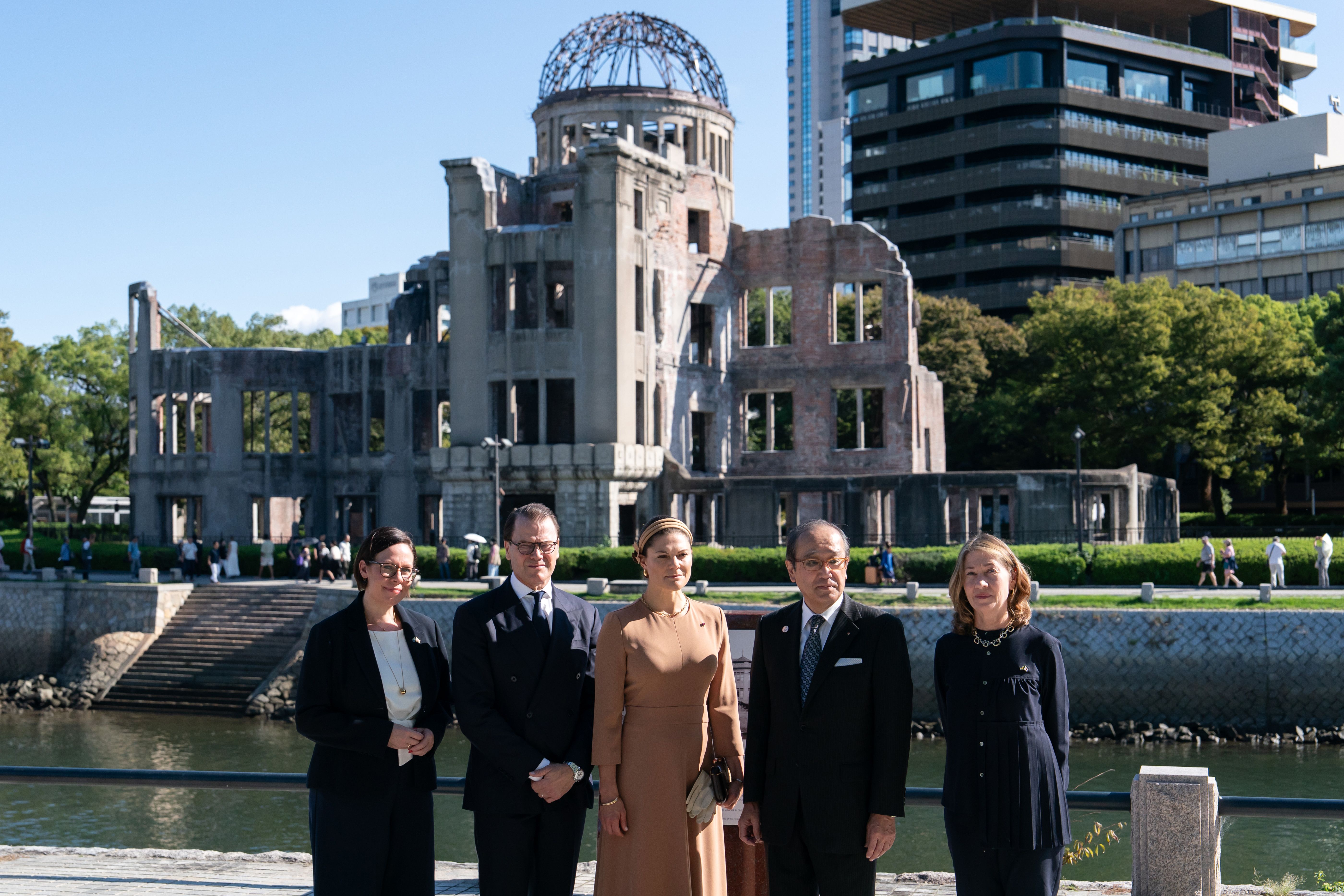 Utrikesminister Maria Malmer Stenergard och Kronprinssesparet tillsammans med Hiroshimas borgmästare Kazumi Matsui och Sveriges ambassadör i Japan Viktoria Li  framför husruin.