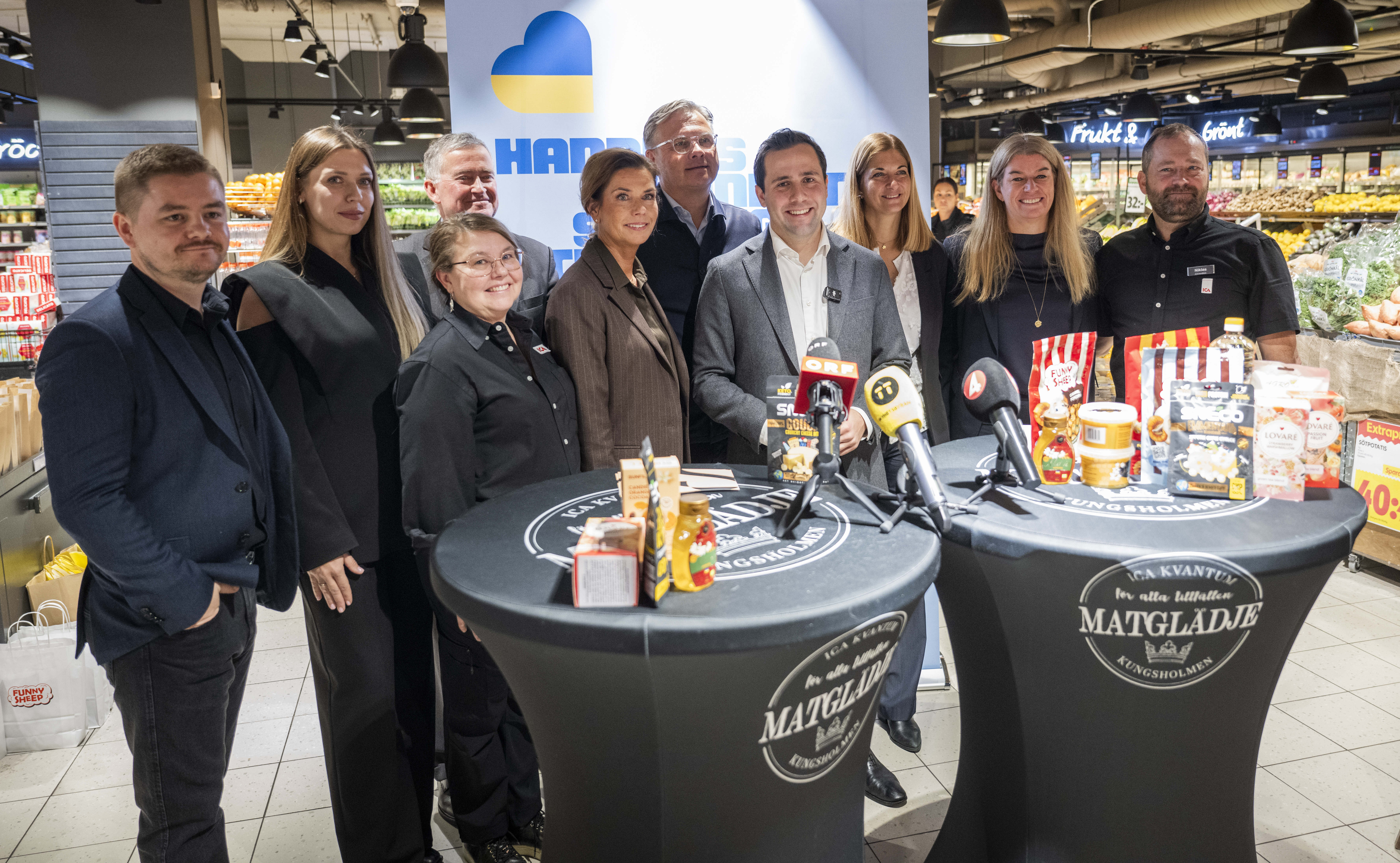 En grupp människor poserar med ukrainska produkter bakom två ståbord.