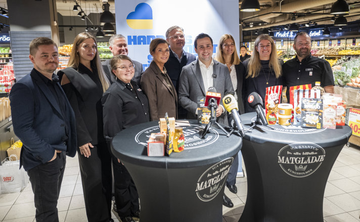 En grupp människor poserar med ukrainska produkter bakom två ståbord.