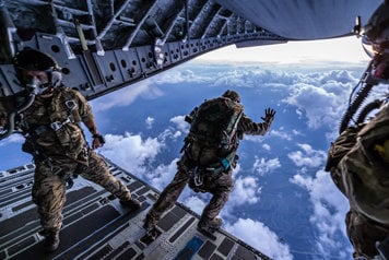 militärklädda fallskärmshoppare hoppar ur ett flygplan