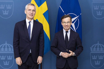 Stoltenberg och Kristersson står bredvid varandra framför flaggor